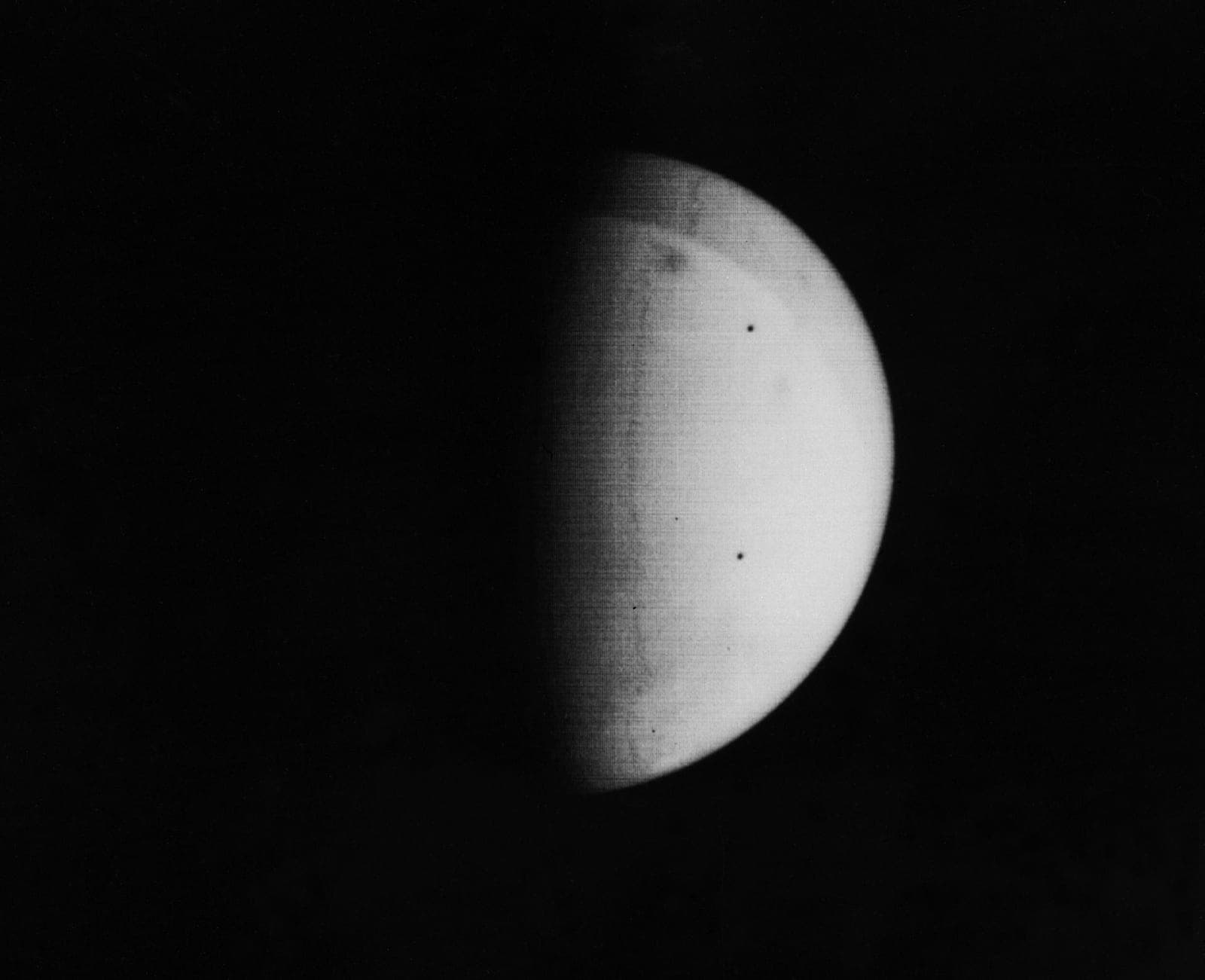 A crescent of Mars almost featureless with dust, with a few dark spots breaking through the haze.