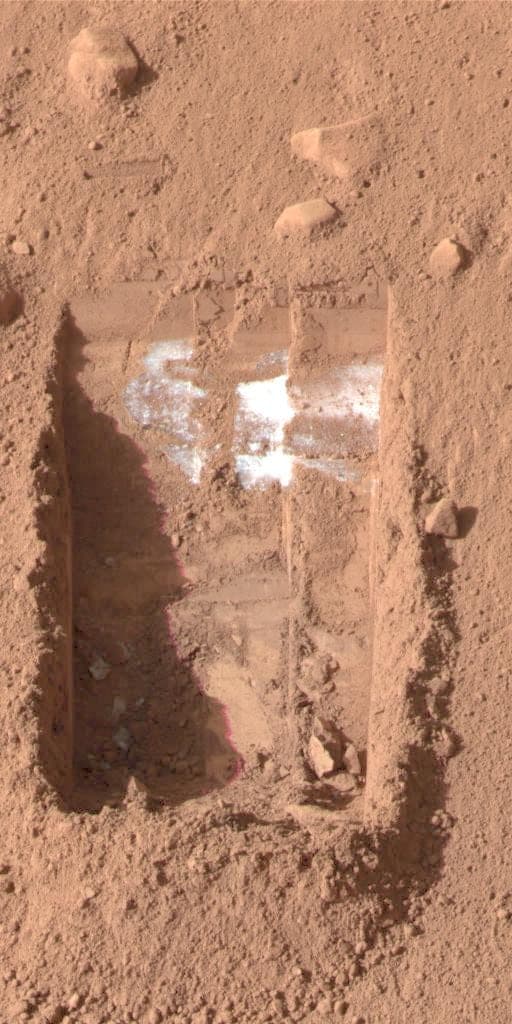 A shallow trench dug into red soil with bright white material exposed at its base.